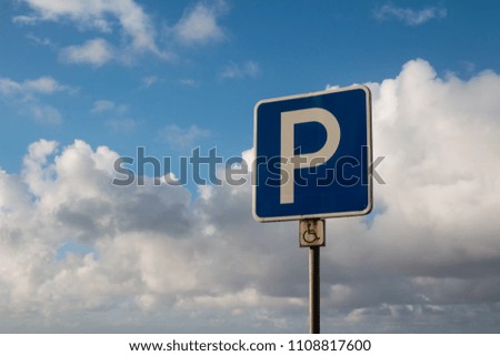 Traffic parking sign for disabled people. Intense white clouds on a blue sky after a night rain.