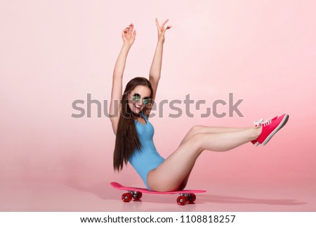 funny woman in blue bodysuit with skateboard on pink background