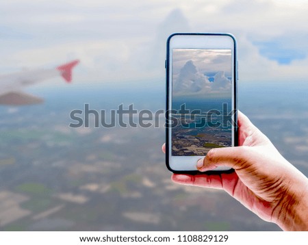 Hand of tourist taking a photo of blue sky, white clouds and wing of airplane with Smartphone | Blurred background | Nature and Travel illustration concept