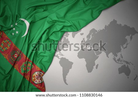 waving colorful national flag of turkmenistan on a gray world map background.