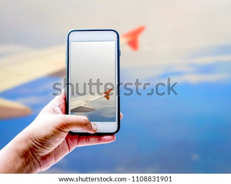 Hand of tourist taking a photo of blue sky, white clouds and wing of airplane with Smartphone | Blurred background | Nature and Travel illustration concept