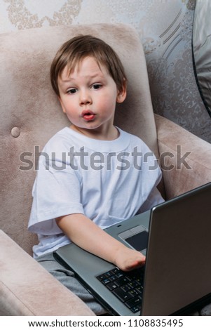 the boy is sitting on a chair and is holding a laptop
