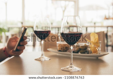 Aperitif with appetizer for two with 2 glasses of red wine - hand of a man distracted by social on his smartphone / mobile phone 