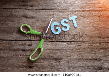 Reducing Government Services Tax concept, scissors cut paper with word GST on wooden background. Selective focus