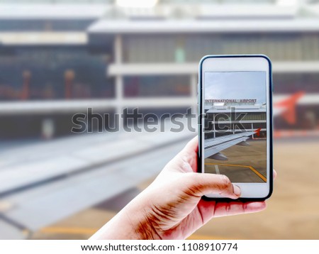 Hand of tourist taking a photo of bulding in airport and wing of airplane with Smartphone | Blurred background | Travel illustration concept
