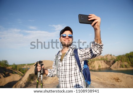 Photo of tourist man with walking sticks photographing himself on mountain hill