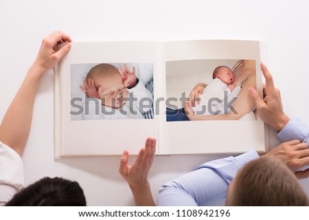 Elevated View Of Couple Looking At Baby's Photo Album On White Background Royalty-Free Stock Photo #1108942196