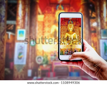 Hand of tourist taking a photo of Buddha Statue and Temple at Luangprabang in Laos with Smartphone | Blurred background | Landmark and Travel illustration concept