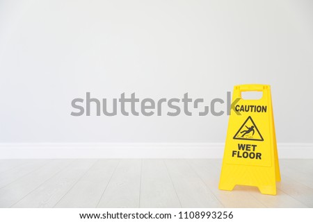 Safety sign with phrase "CAUTION WET FLOOR" on floor near light wall