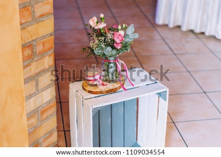 Wedding decoration. A bouquet of colorful flowers in a glass jar. A candle is standing next to it. Decorated with colorful ribbons.