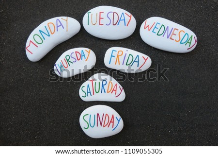 Days of the week carved and painted on sea stones over black volcanic sand
