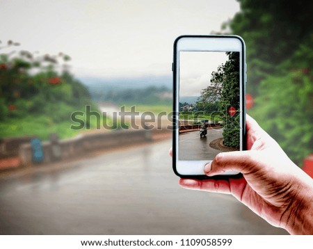 Hand of tourist taking a photo of Namkhan River,mountain and green nature in Laos with Smartphone | Blurred background | Landmark Travel illustration concept