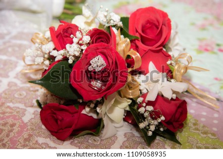 Beautiful toned picture with diamond wedding rings lying on top of a bouquet of red roses
