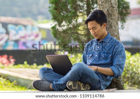 Asian young  man using computer outdoor Royalty-Free Stock Photo #1109114786