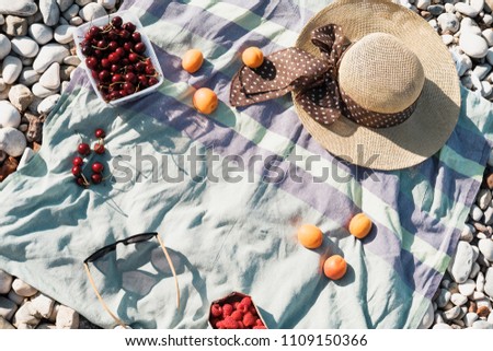 Summer composition with hat, berries and sunglasses on a pebbles beach near sea
