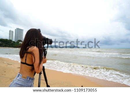 emale photographer with camera taking on tripod,taking a picture of sea and storm,
rainy season  travel concept.