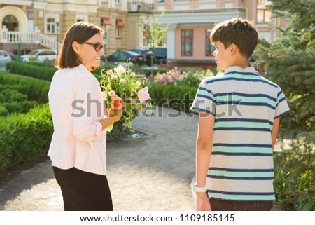 Portrait of woman with bouquets of flowers and teenage boy on city background. Son congratulated his mother.