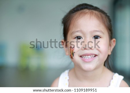 Smiling Asian child girl with butterfly tattoo sticker on cheek