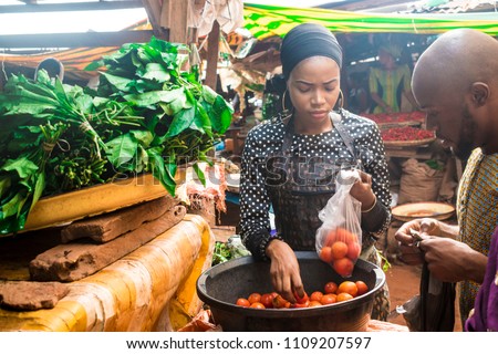 a girl selling tomatoes to a guy in a local african market  Royalty-Free Stock Photo #1109207597