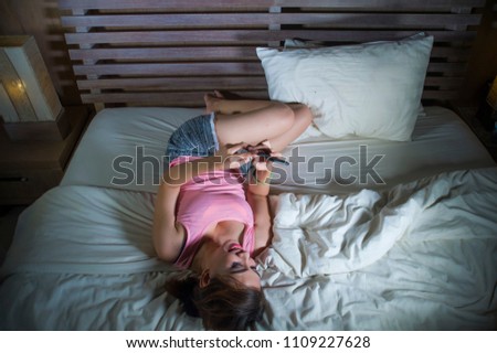 young beautiful and happy girl lying on bed smiling and flirting on internet social media app using mobile phone cheerful and relaxed on her bedroom in on line dating and cellular technology 
