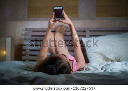 young beautiful and happy girl lying on bed smiling and flirting on internet social media app using mobile phone cheerful and relaxed on her bedroom in on line dating and cellular technology 