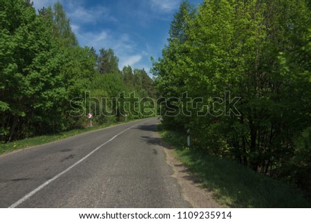 Wide road, green trees and blue sky with gray clouds