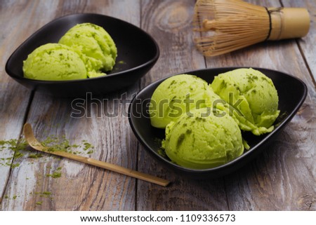Green matcha tea ice cream scoops in dark bowls on wooden background. Copy space