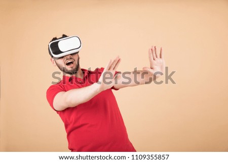Young man wearing a casual outfit and wearing a VR glasses and looking so shocked and screaming, standing on an orange background