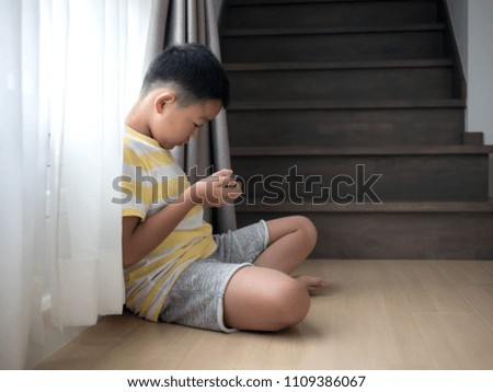 A child sitting on the floor is playing games in a mobile phone.