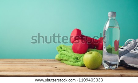 Fitness background with bottle of water, apple, dumbbells and sport shoes on wooden table