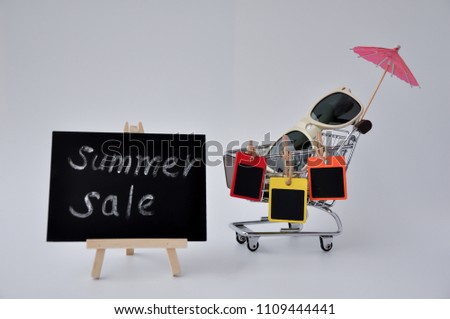 Black board with word summer sale writing on it  with shopping trolley, white sunglasses and umbrella isolated on white background.