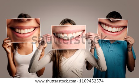 three happy people holding a picture of a mouth smiling on a gray background