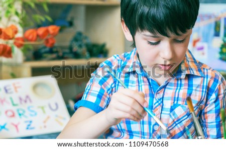 Young boy sitting in front of easel painting a fish, holding a brush in hand. Boy is getting ready to become an artist.