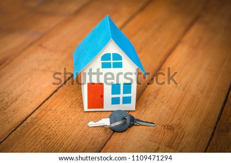 The concept of buying and selling a house. Model house and key on wooden background.