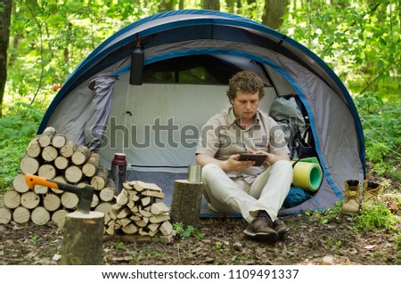 Backpacker uses a tablet outdoors. Spring green forest.