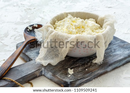 Homemade cottage cheese in cheesecloth and bowl on a white concrete background. Royalty-Free Stock Photo #1109509241