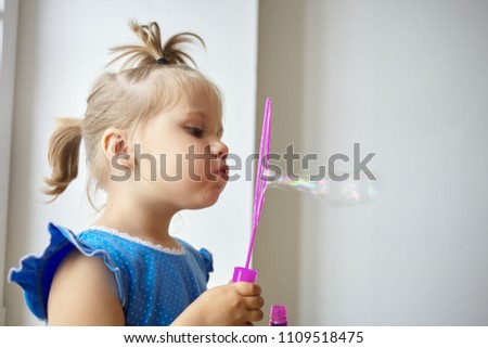 Profile picture of adorable little girl of Caucasian appearance pouting her lips while blowing soap bubbles against white wall background with copy space for your text or advertising information