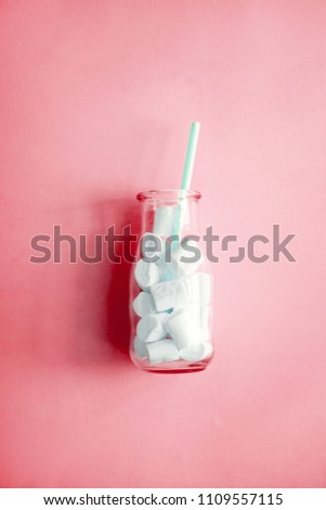 Creative minimalism still life on pastel pink colored background. Glass bottle with marshmallows and straw. Copyspace 