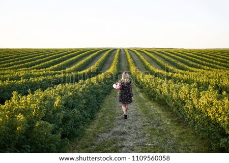 Cute young blonde girl spends time in a picturesque field with a bunch of pions in her hands
