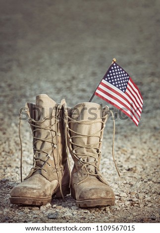 Old military combat boots with the American flag. Rocky gravel background with copy space. Memorial Day or Veterans day concept. Vintage tone.