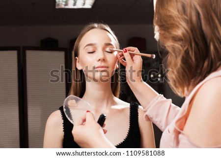 makeup artist appling a primer on an eyelid of a young beautiful model using a brush before dabbing eyeshadows. concept of professional make up training Royalty-Free Stock Photo #1109581088