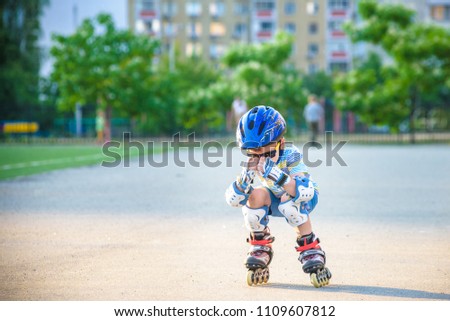 Little boy riding on rollers in the summer in the Park. Happy child in helmet learning to skate.
