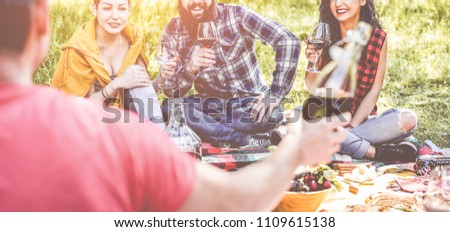 Happy millennial friends doing picnic outdoor in nature - Young people having fun eating and drinking at bbq dinner sitting on grass - Summer lifestyle, food and youth concept - Focus on guys faces