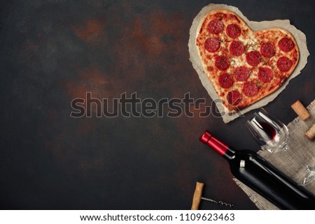 Heart shaped pizza with mozzarella, sausagered with a bottle of wine and wineglas. Valentines day greeting card on rusty background . Top view Royalty-Free Stock Photo #1109623463