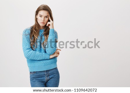 Portrait of bothered bored caucasian female model, holding hand on temple and expressing dislike and annoyance with body language, standing against gray background. How can somebody be so boring