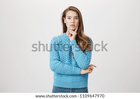 Thoughtful attractive woman holding hand on chin while looking concentrated on some idea she has and standing over gray background. Young scientist looks at board and thinks how to fix her new device