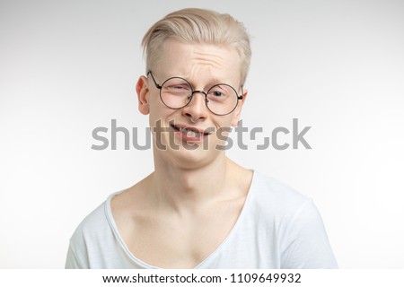 Blonde skeptical young man, in spaectacles with derisive, sneering, scornful, mocking face expression, showing no interest in conversation, isolated on white background. Emotion, facial expression Royalty-Free Stock Photo #1109649932