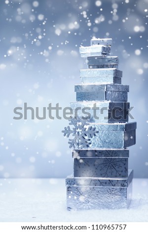 A stacked tower of silver Christmas gifts in diminishing sizes and different angles in falling snow with copyspace