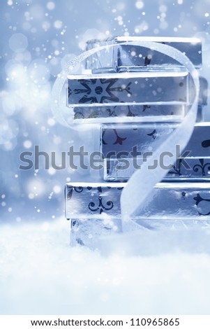 Ethereal festive background with a stack of silver Christmas gift boxes with a decorative ribbon in falling snow