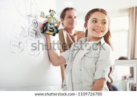 Portrait of happy child comparing toy with picture locating on board during lesson
